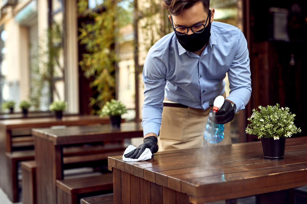 Man sanitizes a table before new guests arrive